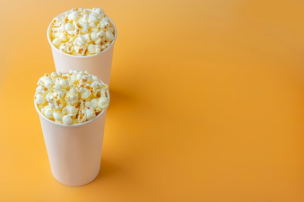 Pop-corn frais dans une boîte blanche sur fond orange. Concept de collation de cinéma. La nourriture pour regarder un film et des divertissements, vue de dessus, mise à plat.