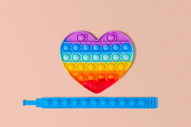 Pop It en forme de coeur arc-en-ciel et bracelet en silicone bleu sur fond beige