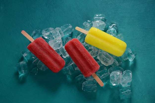 Popsicle aux fraises et popsicle au citron sur fond bleu avec de la glace