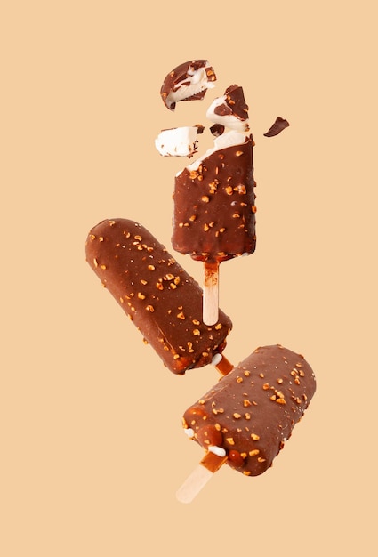 Popsicle blanc en glaçage au chocolat avec des noix volant sur fond beige mise au point sélective