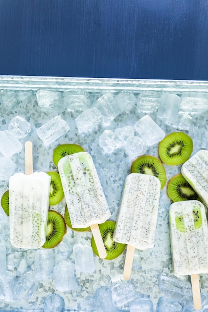 Photo popsicles de chia de noix de coco de kiwi avec le kiwi frais et la glace dans le plateau en métal