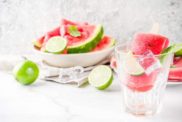 Popsicles doux pastèque d'été et citron vert avec pastèque en tranches et menthe, sur une surface en marbre blanc