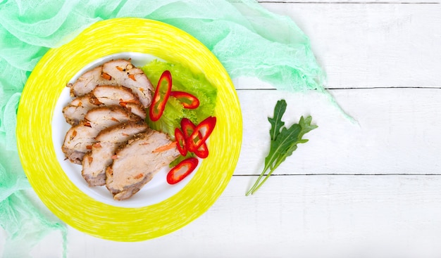 Photo porc au four avec carottes, tranché sur une assiette avec des légumes frais sur la table en bois blanc. vue de dessus, mise à plat. espace de copie.