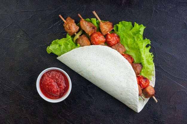 Porc barbecue cuit au four avec des légumes sur des feuilles de laitue dans du pain pita et du ketchup