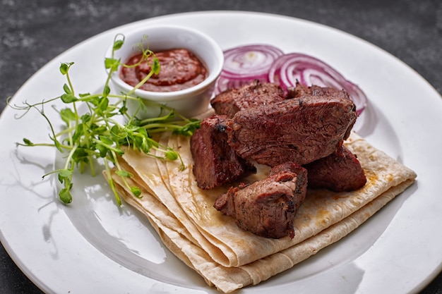 Porc, boeuf, shashlik d'agneau, avec sauce, oignons et lavash, sur une plaque blanche, sur fond sombre