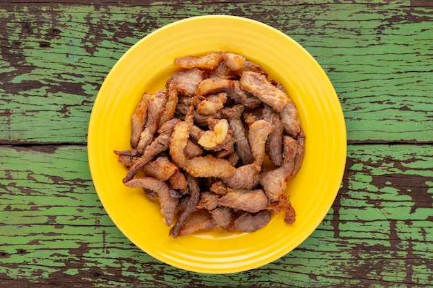 Porc frit savoureux dans une assiette en céramique jaune sur fond de texture de bois naturel vert ancien rustique vue de dessus télévision lay street food