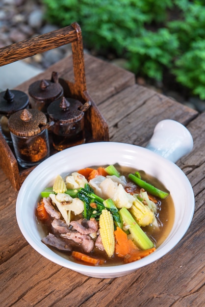 Photo porc garni de chou frisé, carottes, œufs, délicieux, avec garniture, mettre dans une belle tasse en terre cuite, posée sur une table en bois.