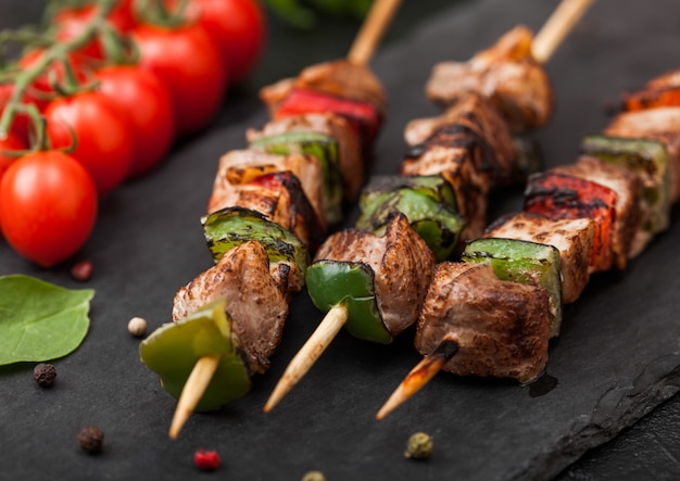 Porc Grillé Et Brochette De Poulet Au Paprika Sur Planche à Découper En Pierre Avec Sel, Poivre Et Tomates Sur Fond Noir