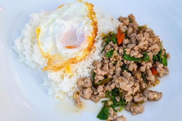 Porc haché au basilic sacré Basilic thaï sauté avec du porc haché et un œuf au plat sur une assiette blanche