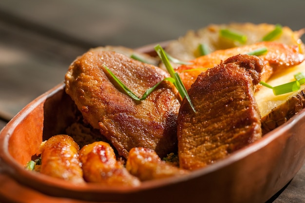 Porc et saucisse dans le bol d'argile accompagnés de tranches d'ananas. Cuisine brésilienne.