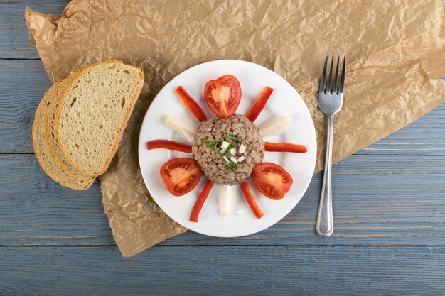 Porridge de sarrasin au service exquis sur fond rustique en bois Vue de dessus. Kasha russe ou blé de sarrasin pseudocéréal cuit décoré de tomates, d'oignons et de légumes verts