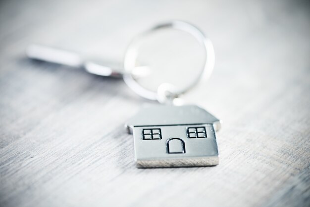 Porte-clés en forme de maison en argent avec clé sur fond de bois se bouchent