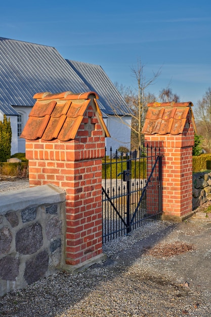 Une porte en fer noir fermée entre deux piliers en briques rouges dans un parc par une journée d'été ensoleillée Entrée extérieure d'une maison ou d'une maison dans une petite ville ou un village avec un ciel bleu en arrière-plan