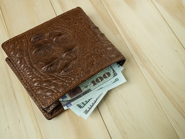 Le portefeuille et le billet en cuir de crocodile sur table en bois.