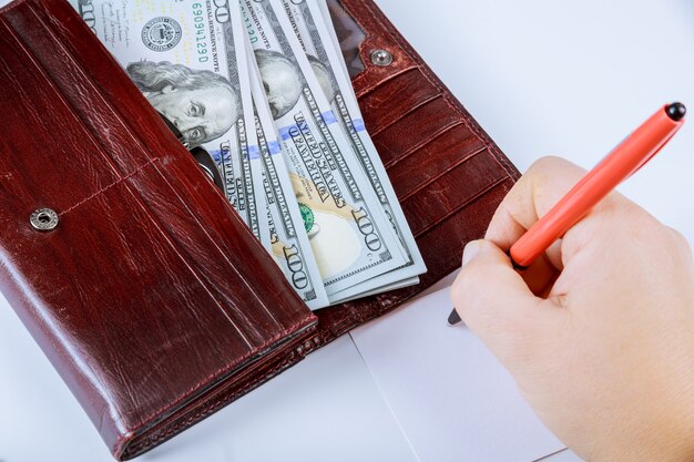 Portefeuille avec des billets de cent dollars sur fond gris. Un stylo et une feuille blanche dans la main de la fille.