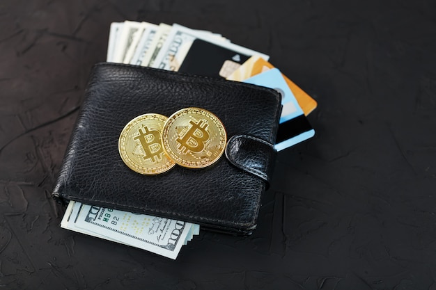 Photo un portefeuille noir avec des dollars, des cartes électroniques et des bitcoins sur fond noir texturé.