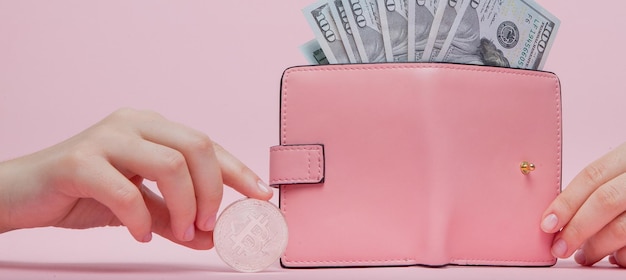 Portefeuille rose avec dollars et bitcoin dans la main de la femme sur fond rose avec espace de copie