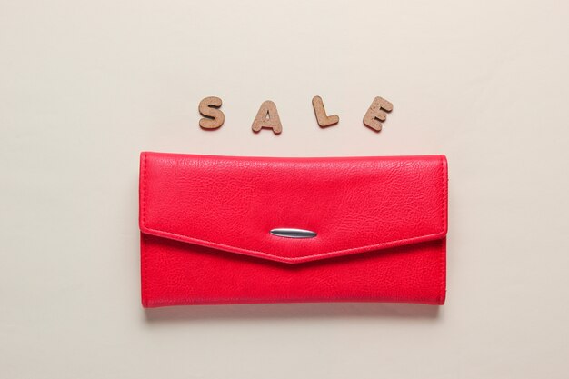 Portefeuille tendance rouge sur une surface beige avec texte SALE.