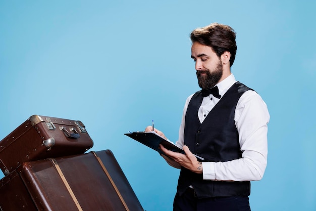 Photo le portier à cravate vérifie les papiers, vérifie les noms des clients de l'hôtel à leur arrivée, le jeune homme à la profession de portier prend des notes sur les fichiers des archives pour garder les preuves sur la caméra.