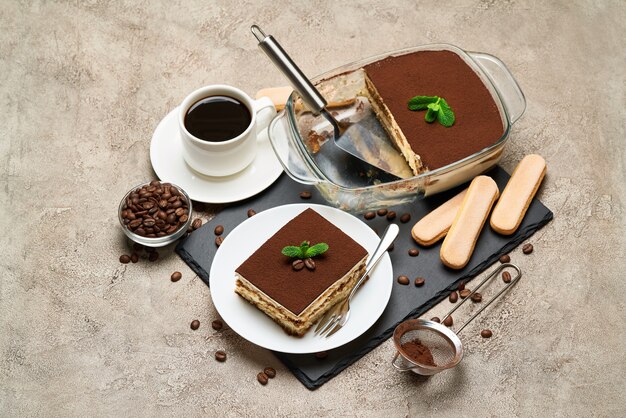 Portion de dessert tiramisu italien traditionnel et cafetière moka sur table en béton gris