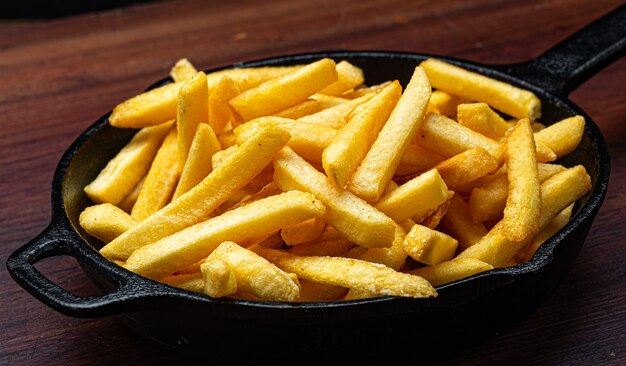 Portion de frites servi dans une poêle en fer sur un fond de bois