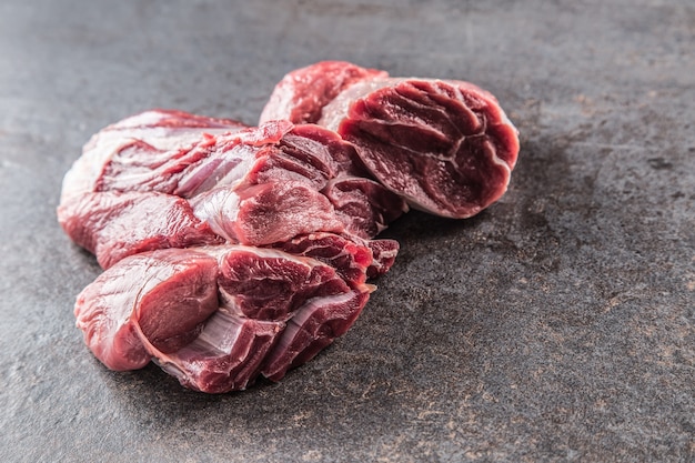 Portion de jarret de boeuf cru sur une planche de boucher sombre.