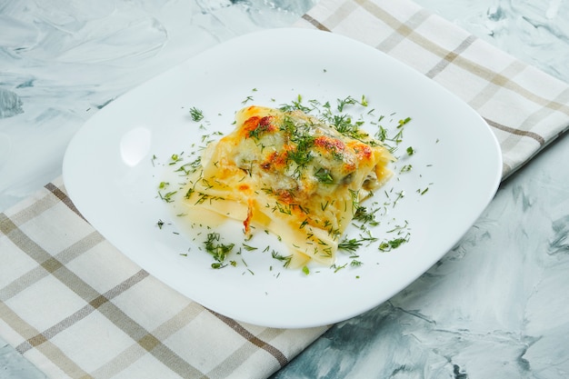 Portion de lasagne italienne maison avec fromage, sauce blanche et poulet sur une plaque blanche avec un chiffon. Pâtes italiennes traditionnelles. Table grise