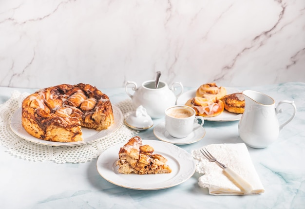 Portion de petits pains à la cannelle faits maison sur une plaque blanche sur une table blanche avec du café et des petits pains à pâtisserie