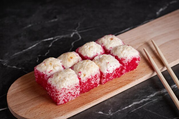 Une portion de petits pains sur un support, de la nourriture japonaise, des sushis sur la table, des baguettes chinoises, un fond sombre