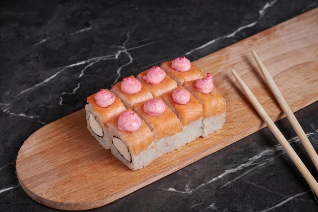 Une portion de petits pains sur un support, de la nourriture japonaise, des sushis sur la table, des baguettes chinoises, un fond sombre