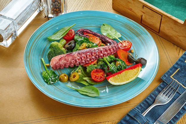 Portion de salade appétissante avec tentacule de poulpe et légumes cuits à la vapeur sur une plaque bleue sur une table en bois. Réglage de la table du restaurant