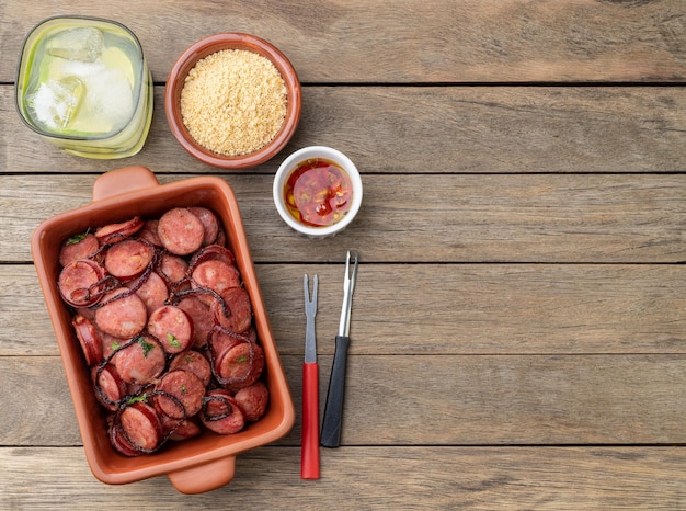 Portion de saucisse calabraise grillée avec farofa à l'oignon et caipirinha sur table en bois avec espace de copie