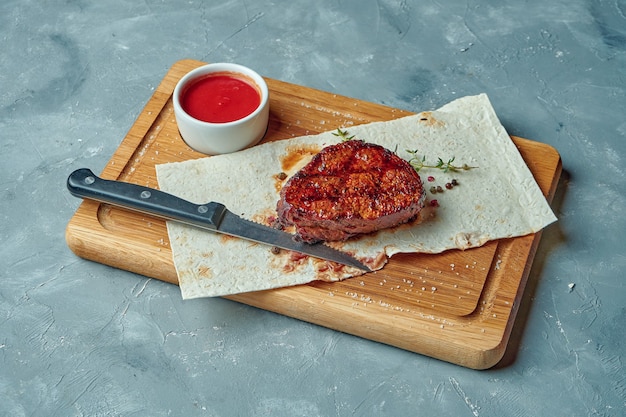 Portion de steak de boeuf cuit au barbecue aux épices sur planche de bois sur surface grise