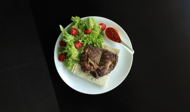 Portion de steak de viande avec sauce et laitue fraîche dans une assiette sur la vue de dessus de la surface noire