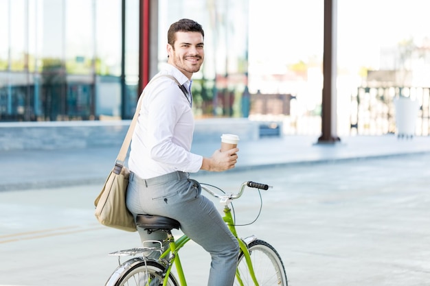 Portrait d'administrateur souriant tout en tenant une tasse jetable et un vélo d'équitation en ville