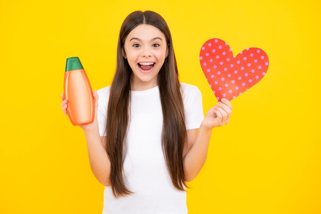 Portrait d'adolescent heureux adolescent enfant fille avec bouteille de shampoing ou gel douche isolé sur fond jaune produit cosmétique pour cheveux enfants fille souriante