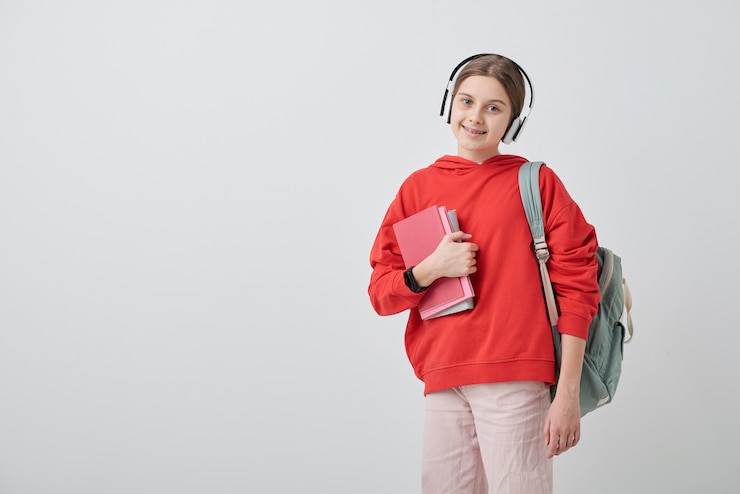 Photo portrait d'adolescent jolie souriante dans les écouteurs portant cartable et tenant des livres scolaires