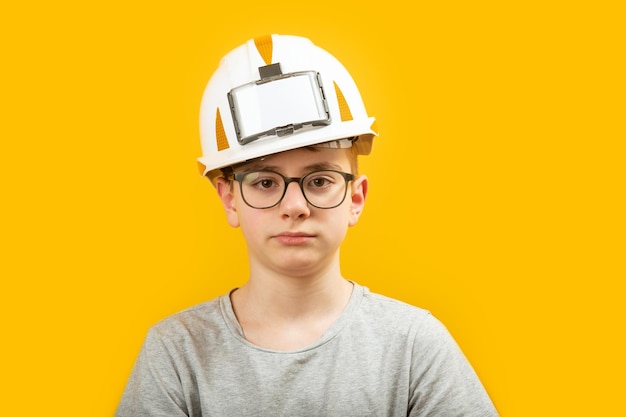 Portrait d'un adolescent portant des lunettes et un casque de protection blanc isolé sur fond jaune L'enfant est comme un constructeur ou un ingénieur