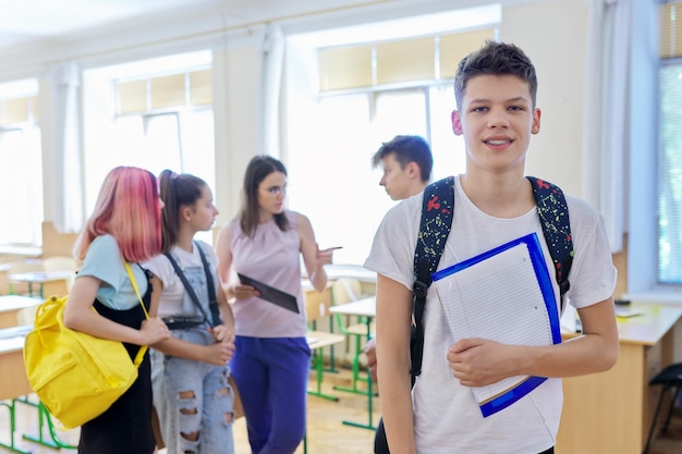 Portrait d'un adolescent regardant la caméra, un étudiant en classe avec un groupe d'enfants d'élèves et une enseignante. Éducation, école, collège, concept d'adolescents