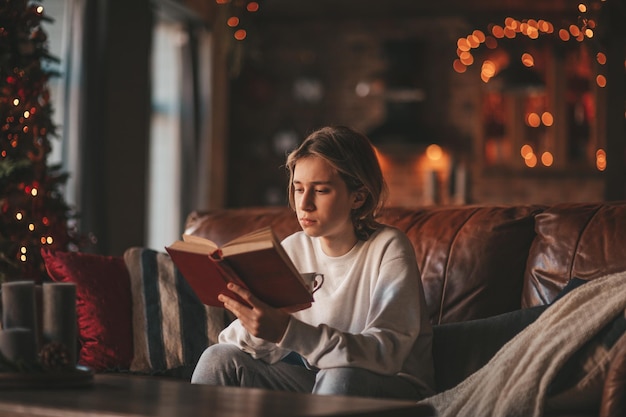 Portrait d'un adolescent souriant authentique et candide, lisant un livre à distance étudiant à la maison Noël