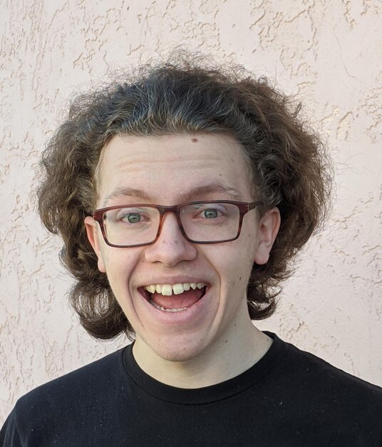 Portrait d'un adolescent souriant avec des cheveux bouclés et des lunettes contre le mur