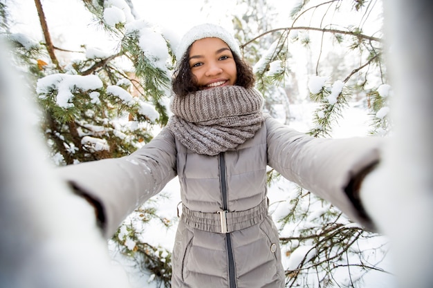 Portrait d&#39;une adolescente adolescent africaine adolescente portant des vêtements chauds prenant le selfie dans la forêt d&#39;hiver, regardant la caméra et souriant