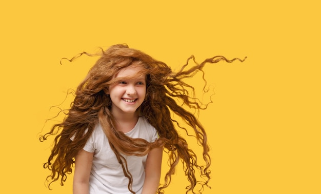 Portrait d'une adolescente aux cheveux aérés en t-shirt blanc sur fond jaune vif.