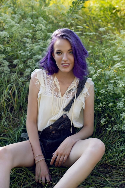 Portrait d'une adolescente aux cheveux violets et une boucle d'oreille dans le nez s'asseoir dans l'herbe dans la nature