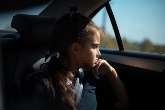 Portrait d'une adolescente sur la banquette arrière de la voiture, regardant la fenêtre.