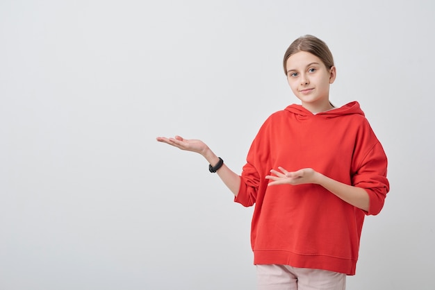 Portrait d'adolescente à capuche rouge gesticulant de côté tout en présentant son idée