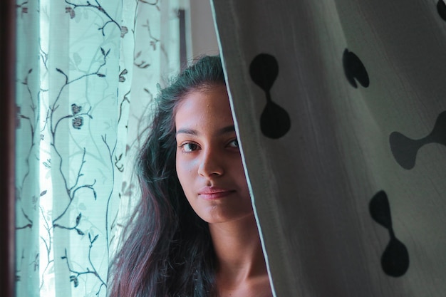 Portrait d'une adolescente debout devant le rideau à la maison