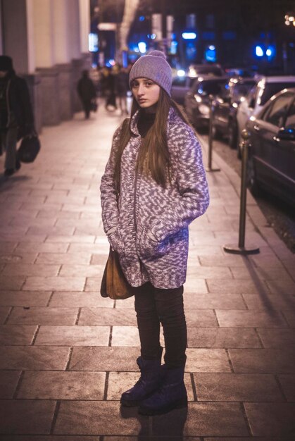 Photo portrait d'une adolescente debout sur le trottoir de la ville la nuit