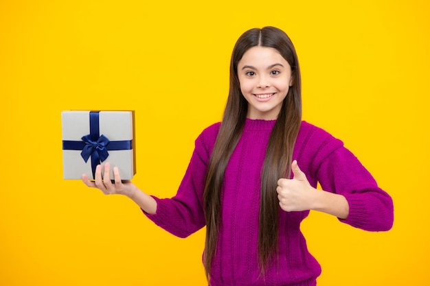 Portrait d'une adolescente enfant fille tenant une boîte présente isolée sur fond de studio jaune Présenter le concept de salutation et de cadeau Concept de vacances d'anniversaire