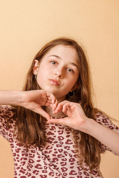 Portrait D'une Adolescente Enfant Montre Un Coeur Sur Un Fond Beige